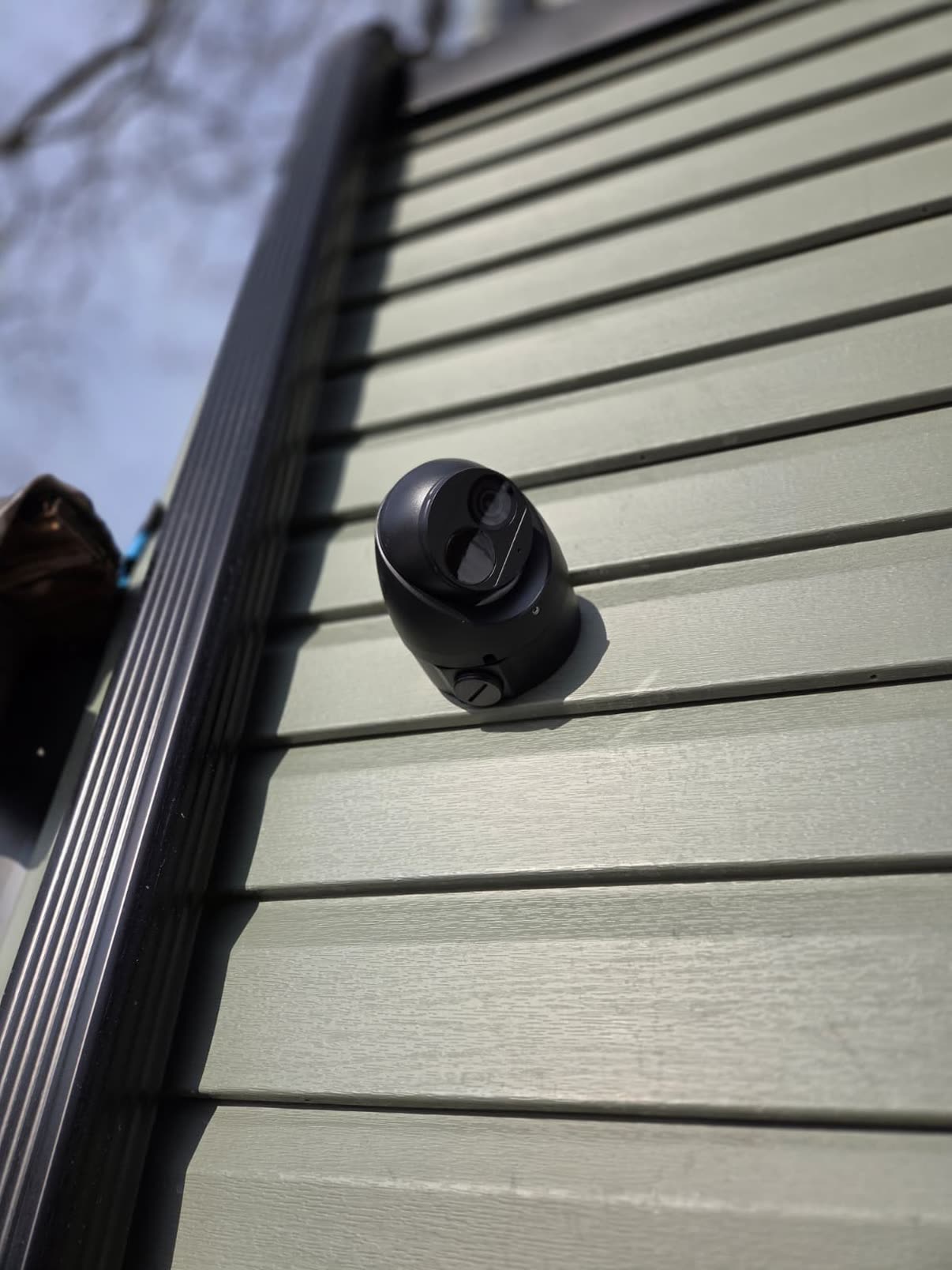 Security camera mounted on green vinyl siding, low-angle view